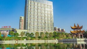 Een hoog hotel met een moderne glazen gevel, gelegen naast een waterpartij met een traditioneel Chinees paviljoen.