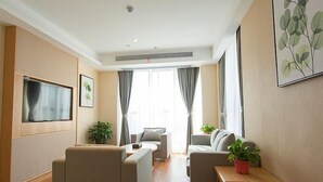Een moderne woonkamer met twee banken, een salontafel, een aan de muur bevestigde televisie en een groot raam met gordijnen.
