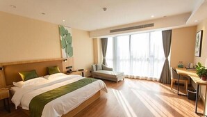 Een moderne hotelkamer met een groot bed, een bureau en uitzicht op de stad door grote ramen.