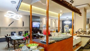 A buffet setup with a red tablecloth, a wooden counter, and various food items. - The Royal Idi (Idi Rayeuk)