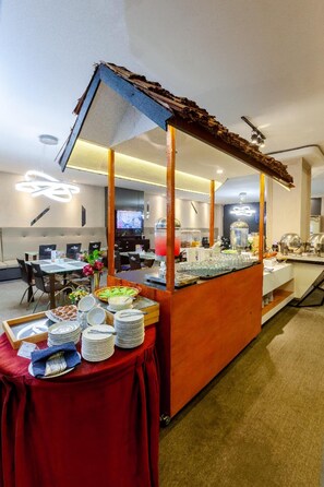A buffet setup with a red tablecloth, a wooden counter, and various food items. - The Royal Idi (Idi Rayeuk)