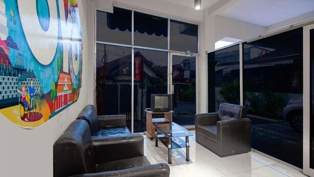 A modern living room with a large TV, comfortable seating, and a colorful mural on the wall. - OYO 3083 D Kost 3 Syariah (Yogyakarta)