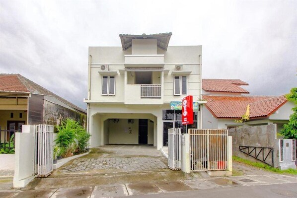 A two-story building with a central entrance, a balcony on the upper floor, and a red flag on the right side. - OYO 3083 D Kost 3 Syariah (Yogyakarta)