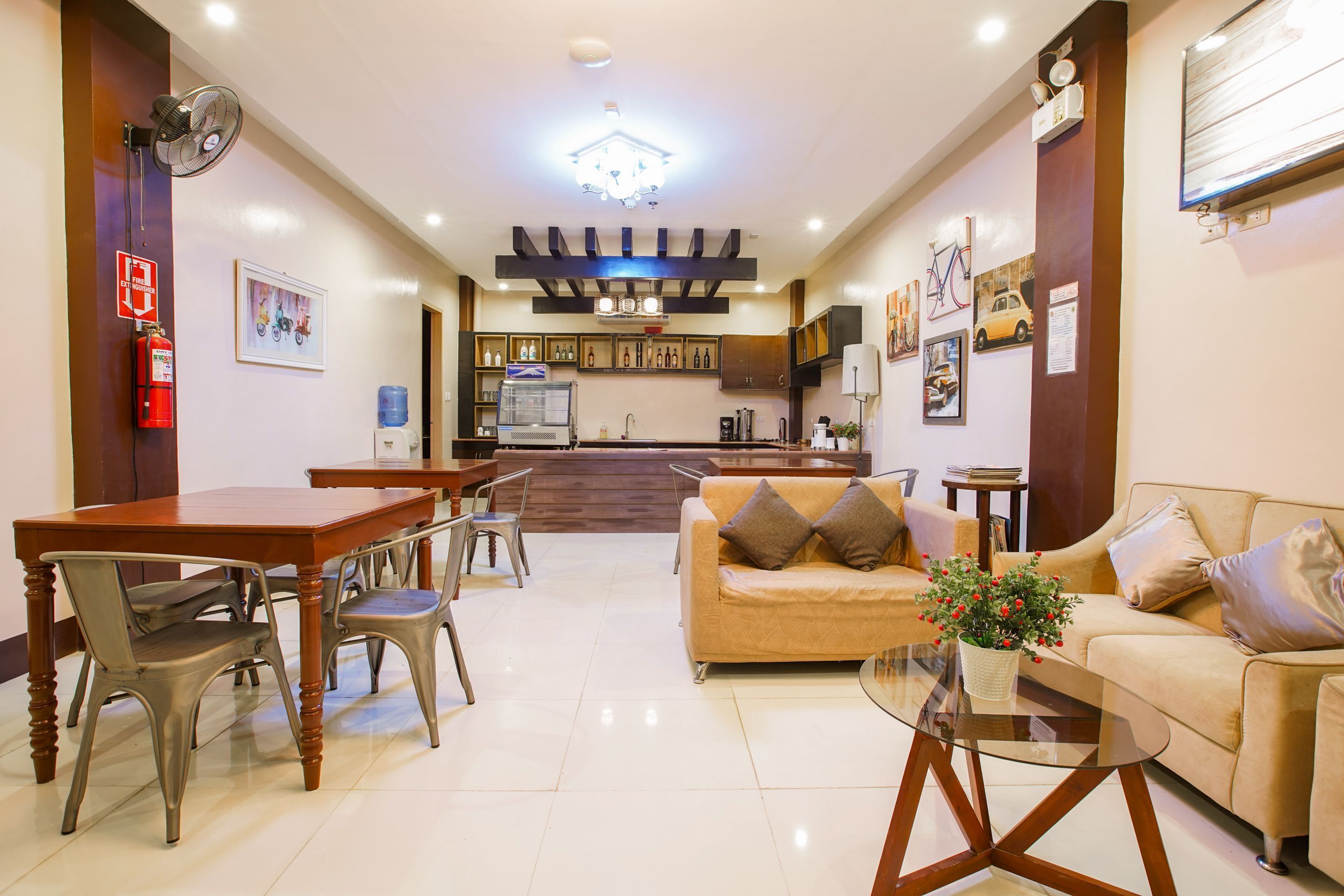 A hotel lobby with a dining area, a sofa, a coffee table, and a kitchen in the background.
