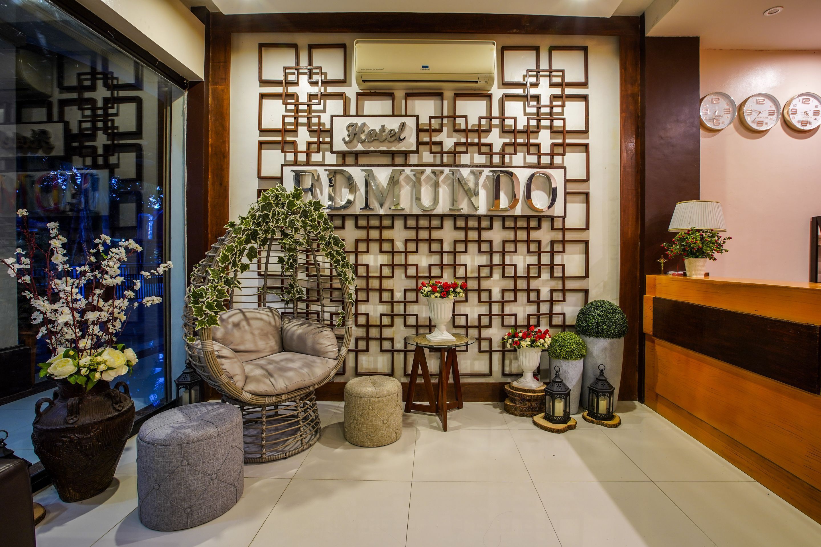A reception area with a 'Hotel' sign, a wicker chair, a potted plant, a small table, and a reception desk.