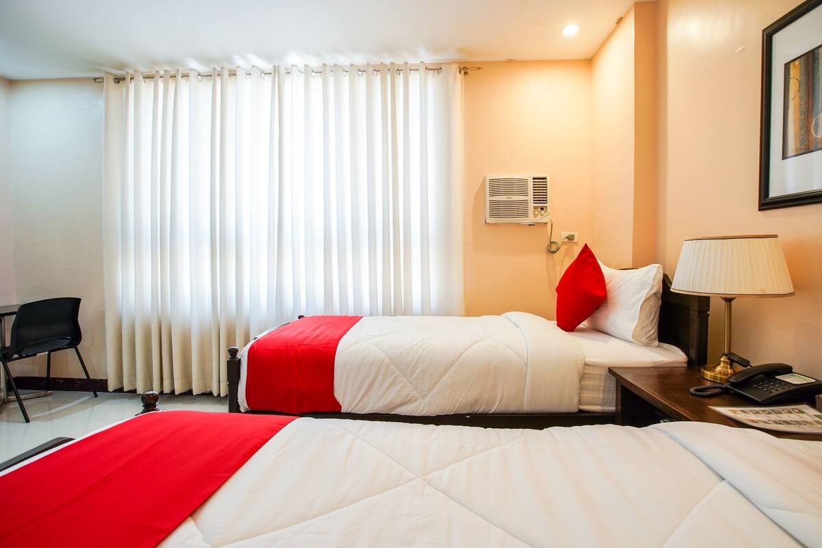 Habitación de hotel con dos camas, un escritorio, una silla, una lámpara, un teléfono y una ventana con cortinas.