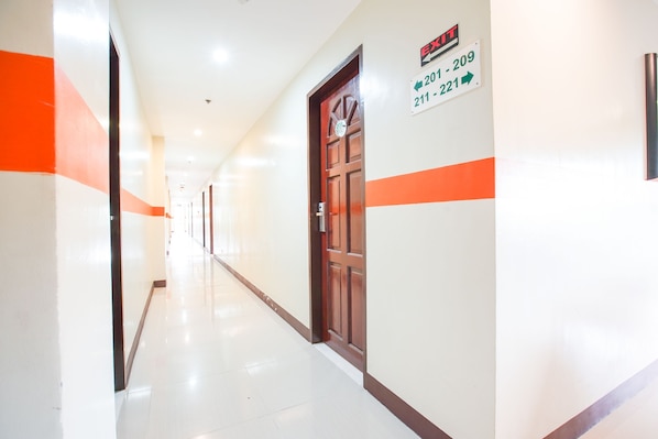 A hallway with a wooden door, white walls, and orange stripes. There are signs indicating room numbers 201-209 and 211-221.