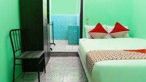 Una habitación con cama, una silla, y un baño visible a través de una puerta abierta, además de baldosas de suelo con un diseño.