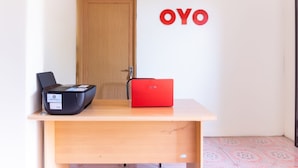 A desk with a black printer and a red laptop in a room with a wooden door and a wall with the letters "OYO" visible.
