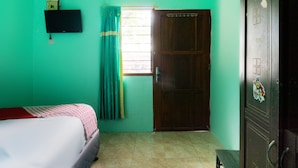 A room with a bed, a window with curtains, a door, and a wall-mounted TV.