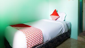 Una cama individual con colcha y almohadas estampadas, una mesita de noche y una pared verde.