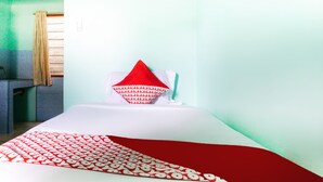 Una cama con una colcha estampada en rojo y blanco, un almohadón rojo y un almohadón blanco en una habitación con paredes verde claro y una ventana con cortinas.