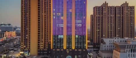 A hotel with a prominent sign, multiple floors, and a parking area in the foreground.