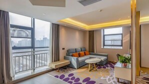 A modern living room with a sofa, a small table, and a view of the city through large windows. - Lavande Hotel (Heze Dingtao) (Heze)