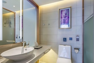 Un baño moderno con un lavamanos ovalado grande, un espejo, una obra de arte enmarcada en la pared y un inodoro con dispensador de toallas.