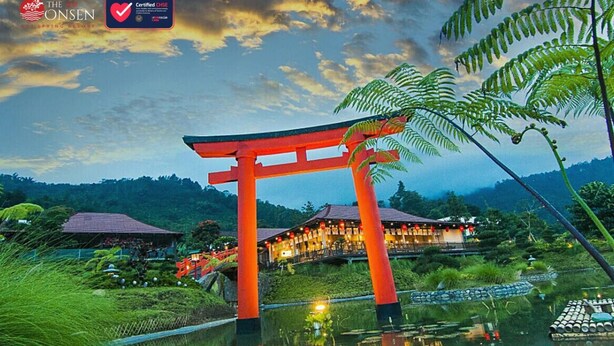 A traditional Japanese torii gate at dusk, with a resort in the background and a body of water reflecting the scene.