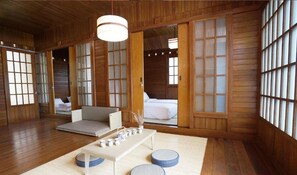 Una tradizionale stanza in stile giapponese con pavimento in tatami, un tavolino con cuscini e porte scorrevoli con pannelli in vetro.