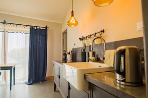 Una cocina moderna con un lavamanos, hervidor y utensilios, además de un ventanal con cortinas.