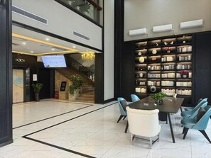 A spacious lobby with a modern staircase, a large bookshelf, and a dining area with chairs and a table. - Xana Hotelle (Dongguan Chang'an) (Dongguan)