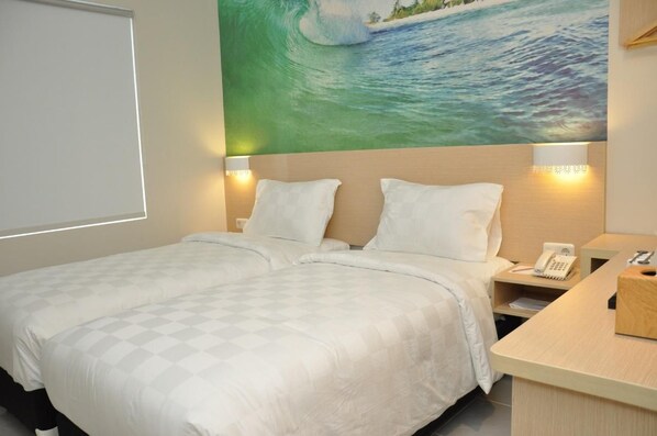 A hotel room with a bed, two bedside lamps, a nightstand with a phone, and a painting of a wave on the wall.