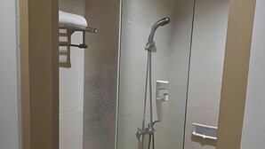 Un baño moderno con mampara de vidrio, ducha con cabezal de ducha manual e inodoro.