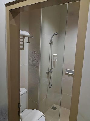 Un baño moderno con mampara de vidrio, ducha con cabezal de ducha manual e inodoro.