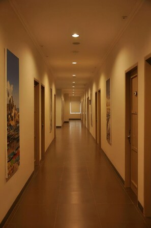 Un couloir d’hôtel avec des portes de chaque côté, un sol carrelé et un éclairage encastré.