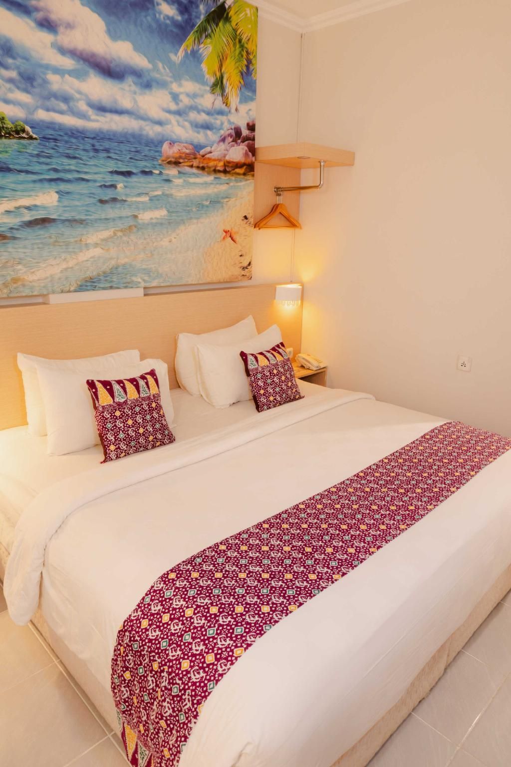 Une chambre d’hôtel avec un grand lit, une table de chevet, une lampe et un tableau représentant une scène de plage.
