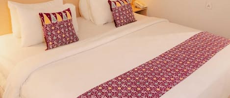 A hotel room with a large bed, a nightstand, a lamp, and a wall painting of a beach scene.