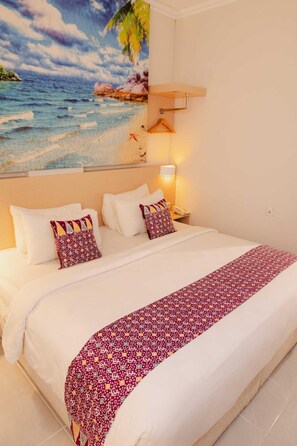 A hotel room with a large bed, a nightstand, a lamp, and a wall painting of a beach scene. - Cordela Hotel Pangkal Pinang (Pangkalpinang)
