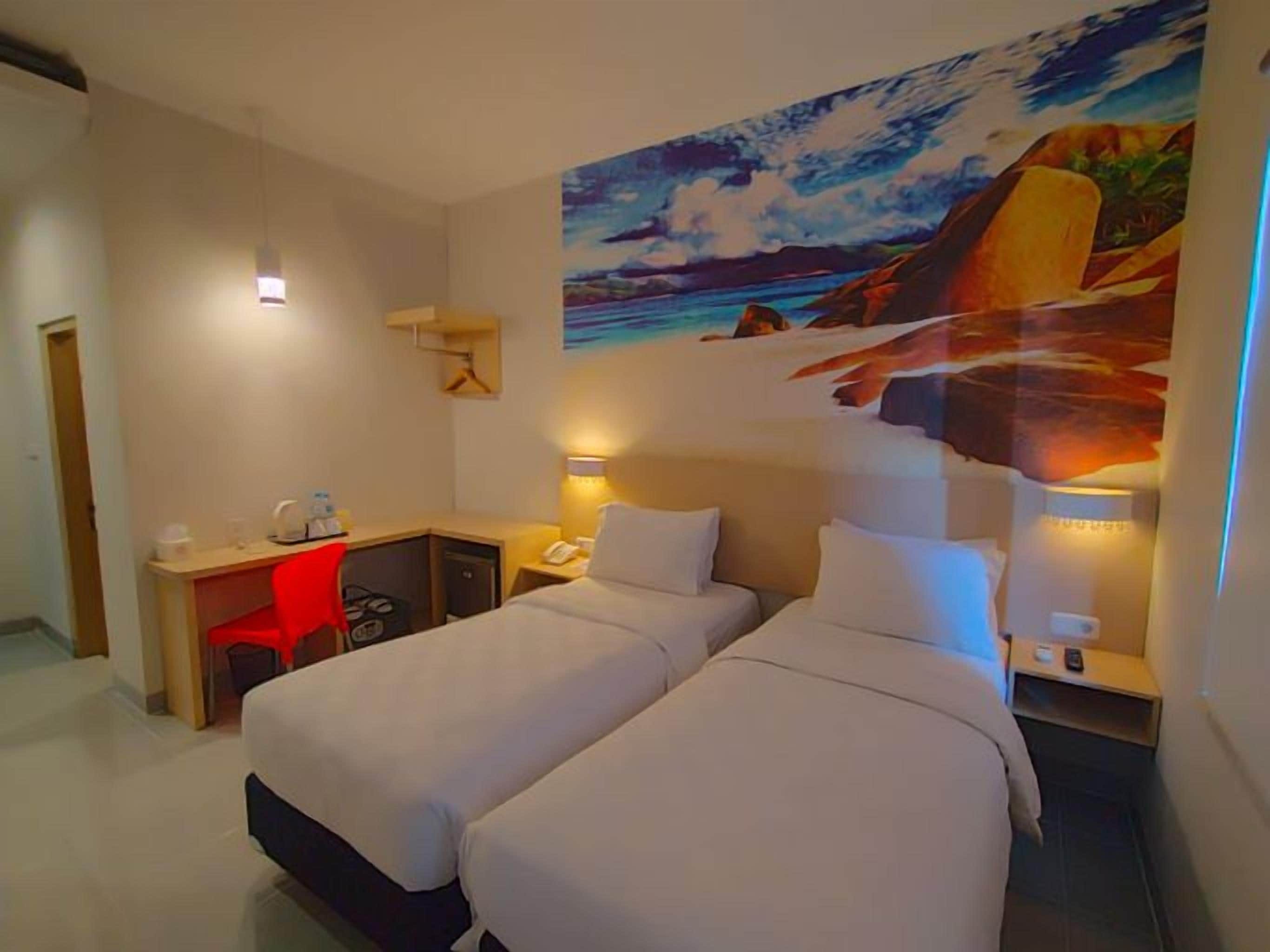 A hotel room with two beds, a desk, a chair, and a painting of a beach scene.