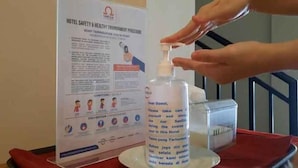 A hand dispensing sanitizer from a bottle next to a hotel safety and hygiene procedure poster. - Cordela Hotel Pangkal Pinang (Pangkalpinang)