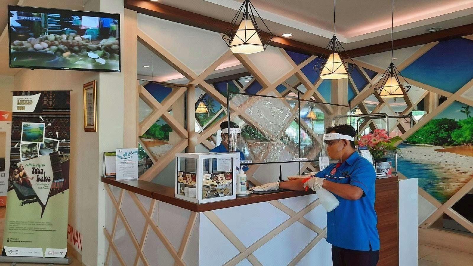 Un espace d’accueil d’hôtel comprenant un comptoir, un téléviseur fixé au mur et une grande fenêtre donnant sur une plage.