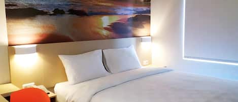 A hotel room with a bed, two bedside lamps, a desk with a chair, and a large wall painting.