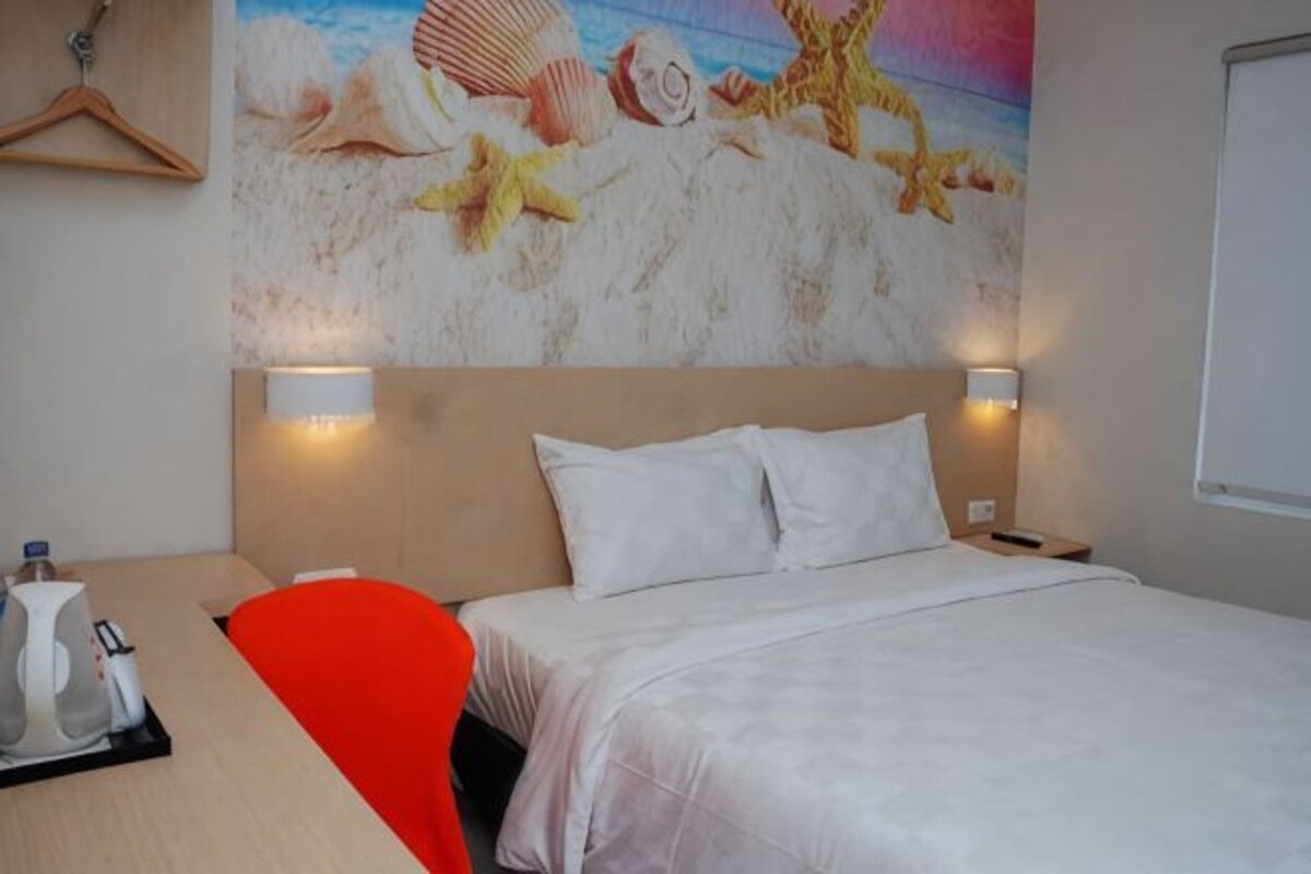 Habitación de hotel con cama, dos lámparas de noche, una mesita de noche, un escritorio con silla y un cuadro en la pared.