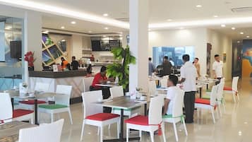 A modern dining area with white chairs and tables, a counter with staff, and a large window providing natural light.
