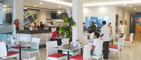 A modern dining area with white chairs and tables, a counter with staff, and a large window providing natural light.