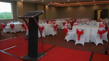 A conference room with multiple round tables, each with white tablecloths and red sashes, and a podium in the foreground.