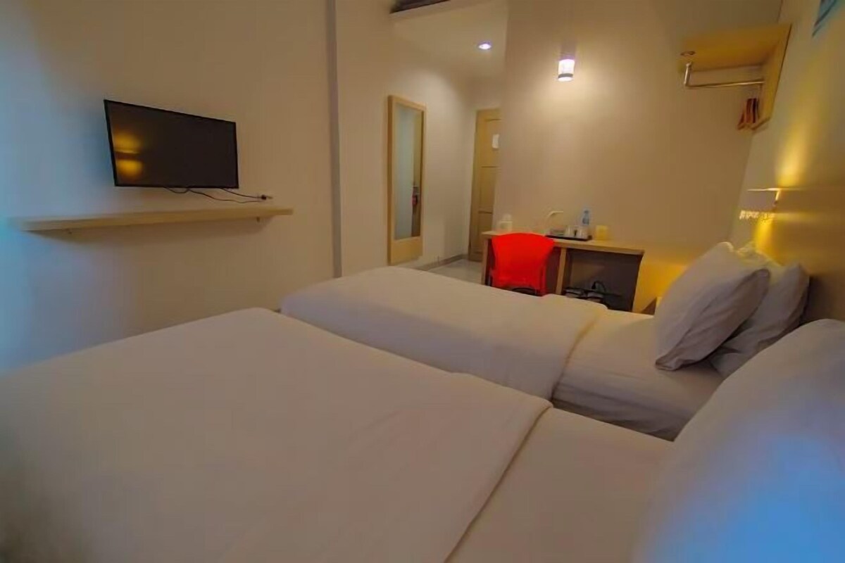 Una habitación de hotel con dos camas, un televisor montado en la pared, un escritorio con una silla y un espejo.
