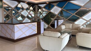 Un vestíbulo moderno con una mesa de recepción, zona de estar y un amplio ventanal con un mural tropical.