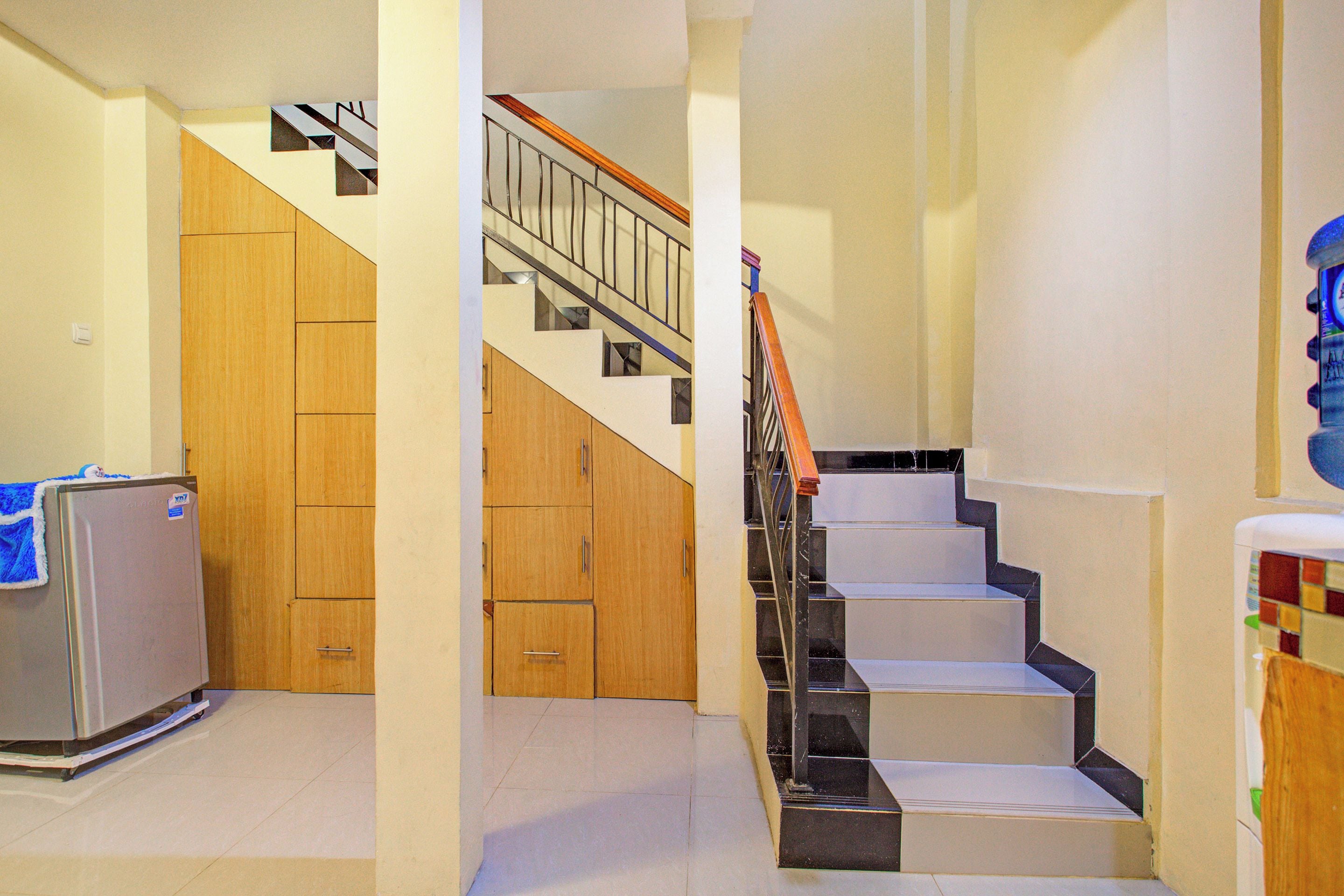A hallway with a refrigerator, wooden cabinets, and a staircase with a metal railing.