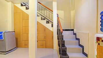 A hallway with a refrigerator, wooden cabinets, and a staircase with a metal railing.