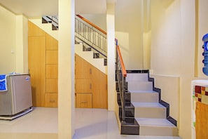 A hallway with a refrigerator, wooden cabinets, and a staircase with a metal railing. - OYO 3148 Sofia Homestay Syariah (Dramaga)