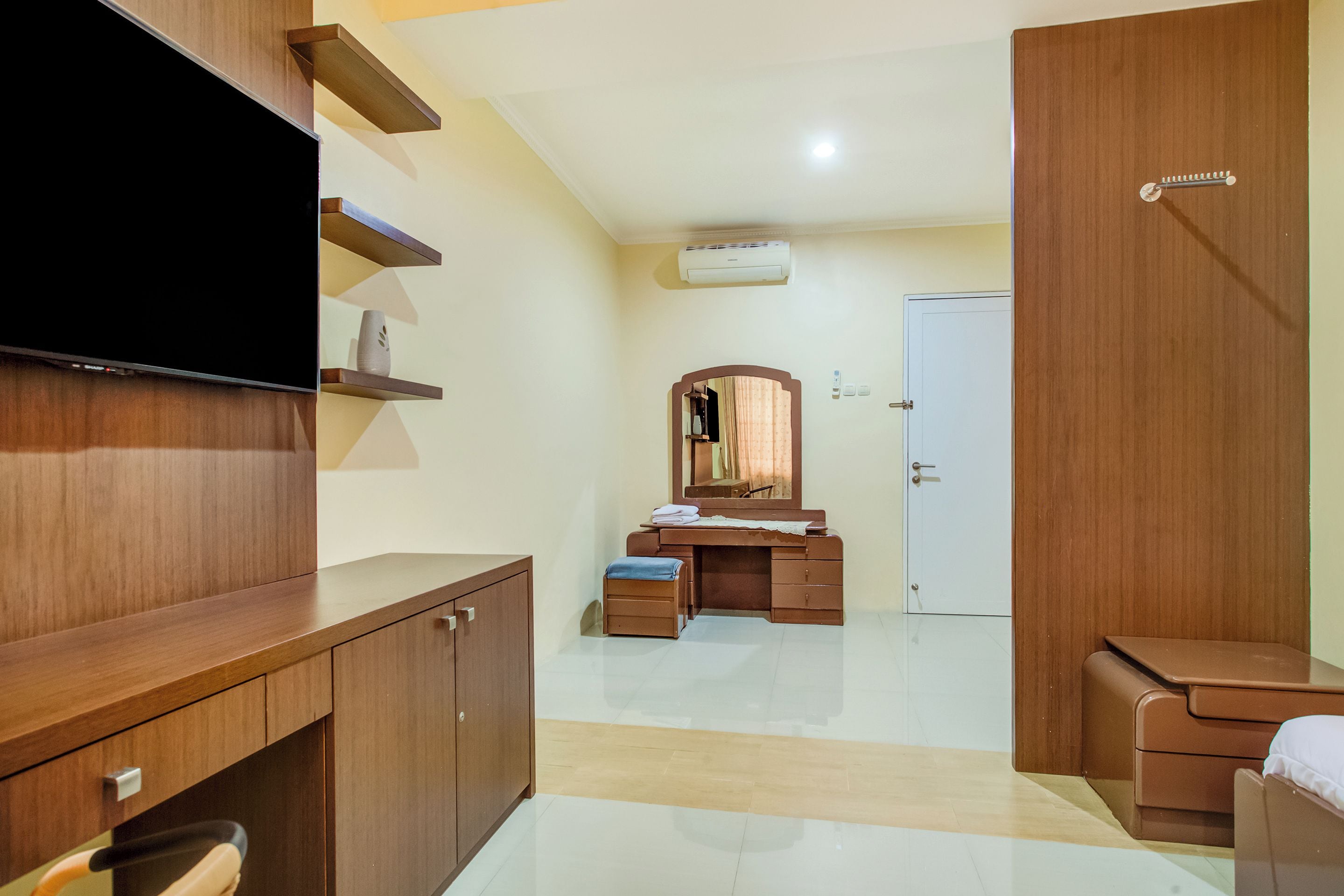 A hotel room with a wooden wardrobe, a flat-screen TV, a vanity with a mirror, and a white door.