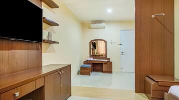 A hotel room with a wooden wardrobe, a flat-screen TV, a vanity with a mirror, and a white door.