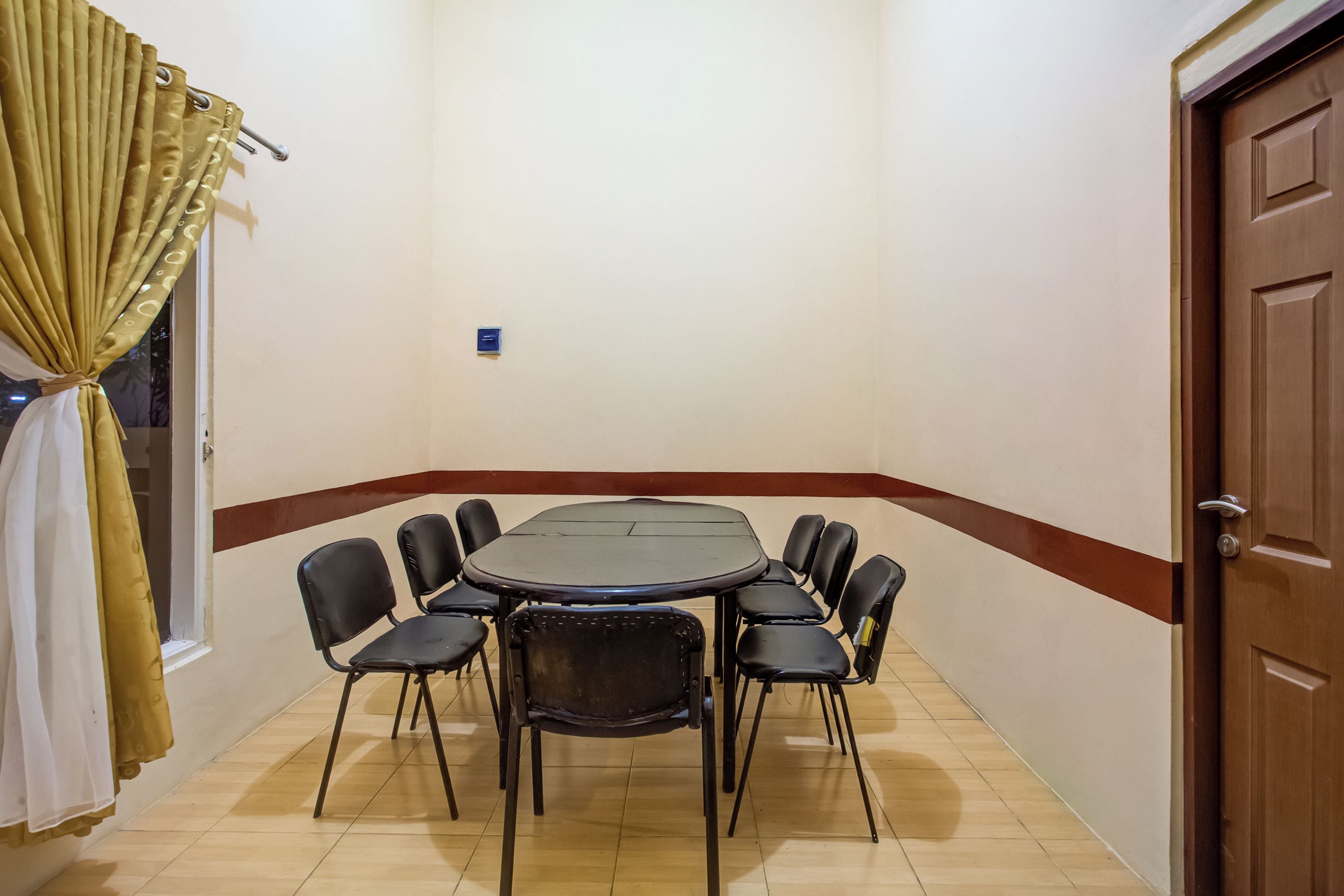 A room with a round table and eight chairs, a door, and a window with curtains.