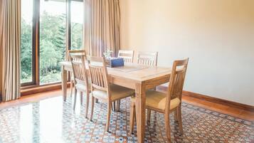 A dining area with a wooden table and chairs, large windows with curtains, and patterned floor tiles.