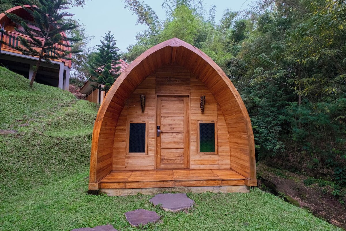 Una cabaña de madera con techo inclinado, dos ventanas y una puerta.
