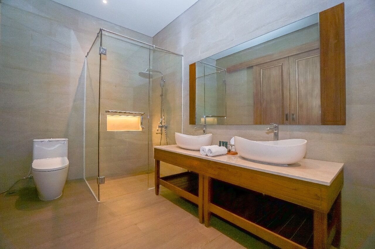A modern bathroom with a glass-enclosed shower, two sinks, a toilet, and a large mirror.