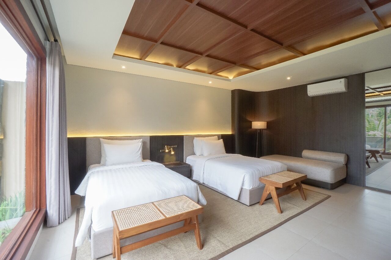 Une chambre d’hôtel moderne avec deux lits, un canapé, une petite table et une grande fenêtre.